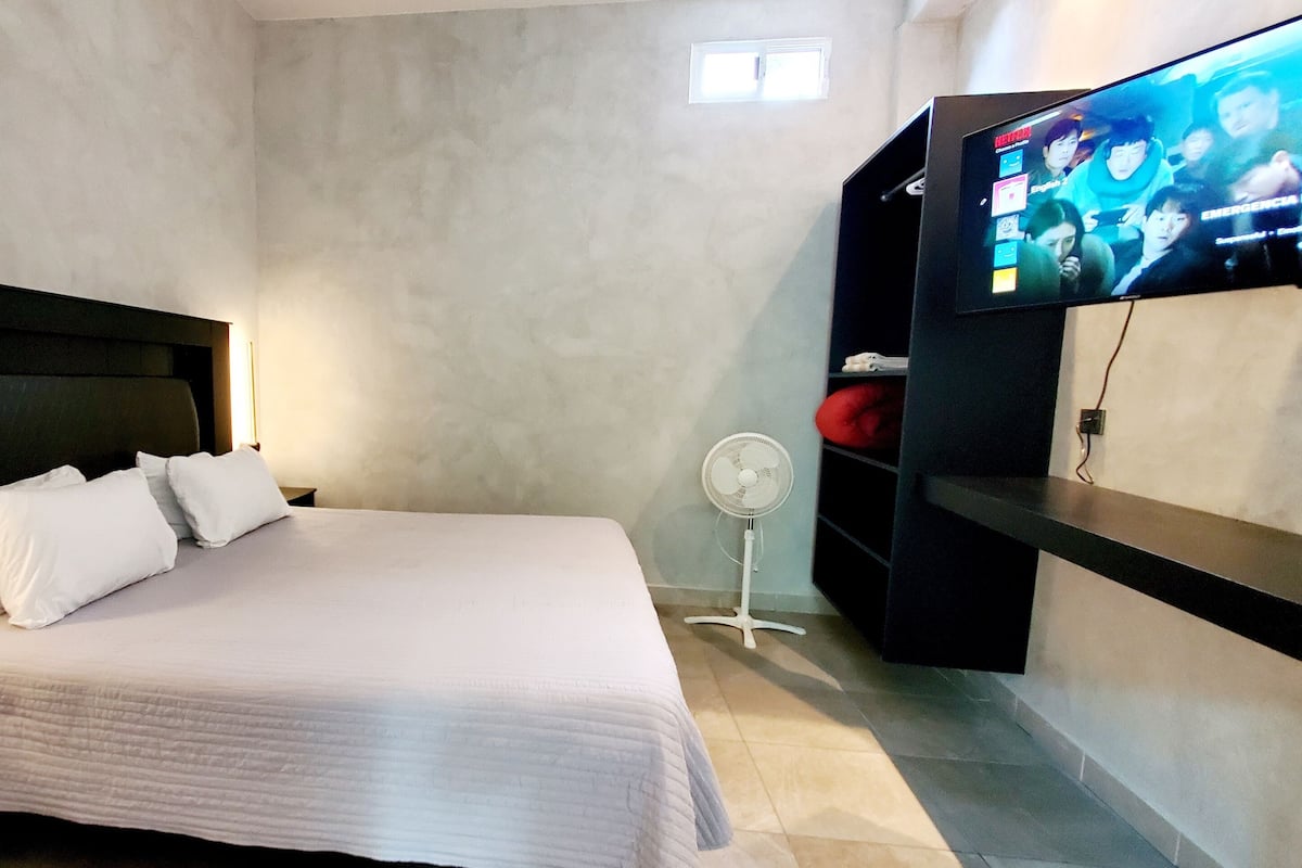 Ein Schlafzimmer mit einem Bett, einem an der Wand montierten Fernseher, einem Nachttisch und einem Wandregal.