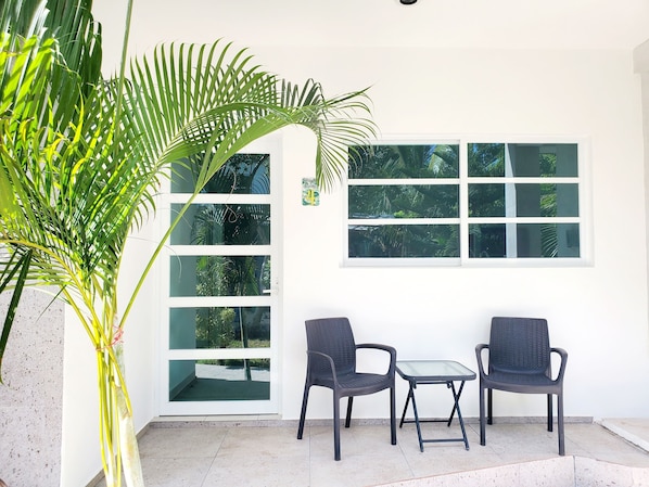 A room with a white wall, a large window, two chairs, a small table, and a potted plant.