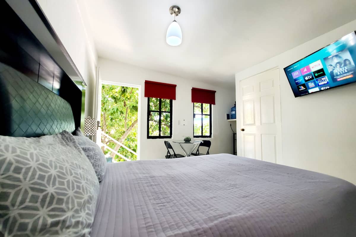 Ein Schlafzimmer mit einem Bett, einem an der Wand montierten Fernseher und einem Fenster mit roten Vorhängen.