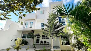 Un edificio moderno di due piani con un balcone, circondato da vegetazione rigogliosa e palme.