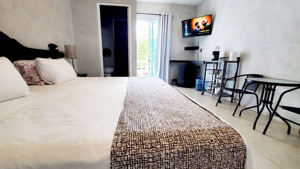 Una camera d'albergo con un letto grande, una TV fissata al muro, una scrivania con sedie e vista sull'esterno.