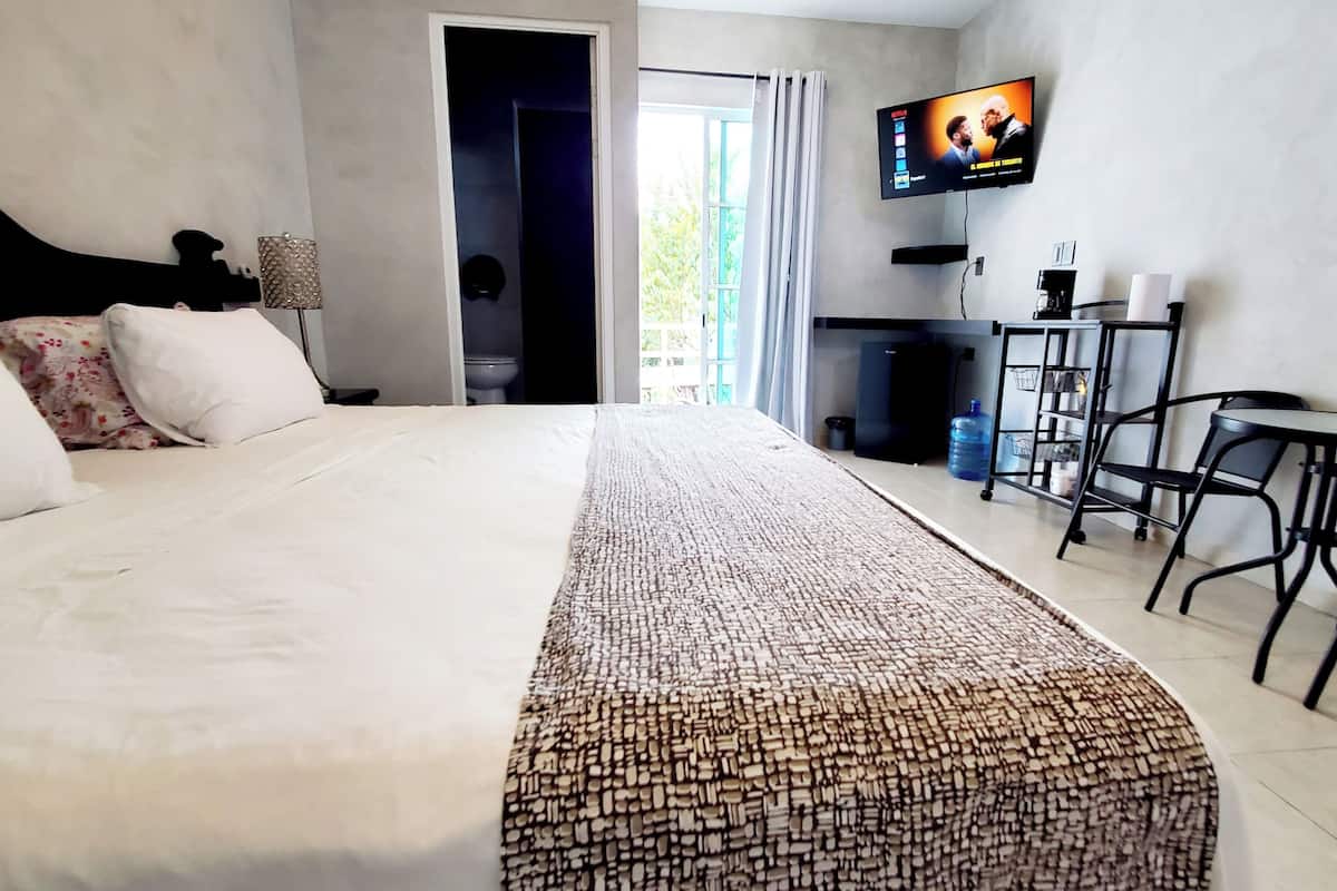 Ein Hotelzimmer mit einem großen Bett, einem an der Wand montierten Fernseher, einem Schreibtisch mit Stühlen und Blick ins Freie.