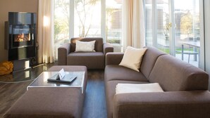 A modern living room with a fireplace, a sofa, a coffee table, and large windows. - Autorenhaus Franz Kafka (Heringsdorf)