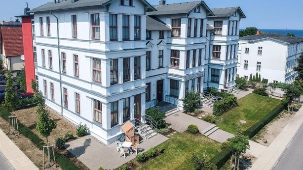 A multi-story building with a classic architectural style, featuring a prominent entrance with steps and a covered outdoor seating area. - Autorenhaus Franz Kafka (Heringsdorf)