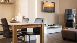 A modern living room with a wooden dining table, black leather chairs, a white sofa, and a flat-screen TV mounted on the wall. - Autorenhaus Franz Kafka (Heringsdorf)