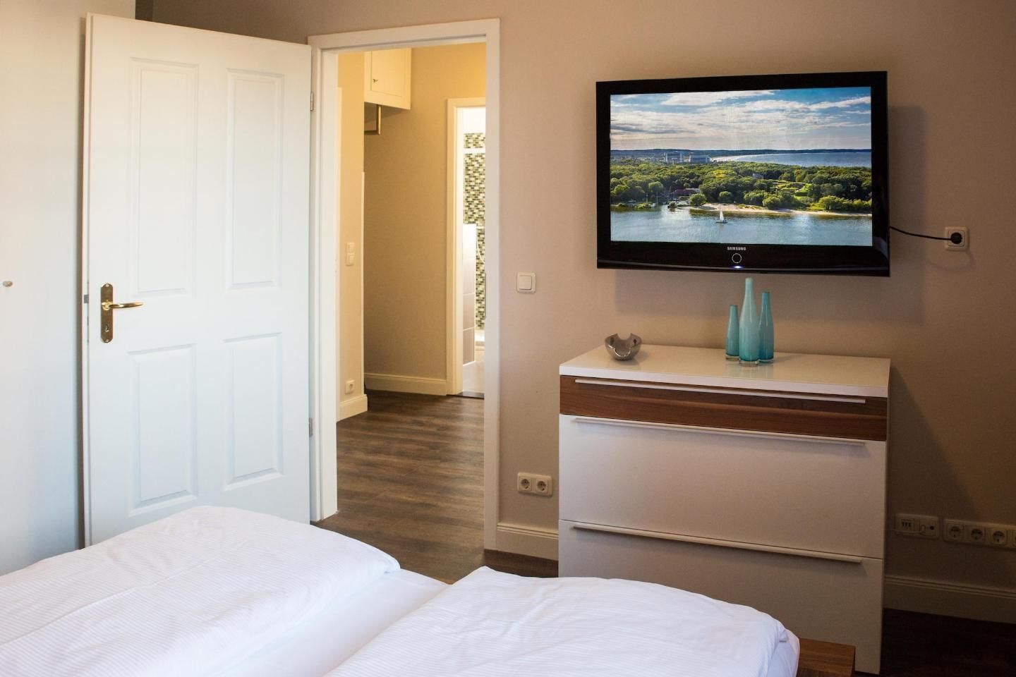Habitación de hotel con cama, televisión montada en la pared y vista a un lago desde la ventana.