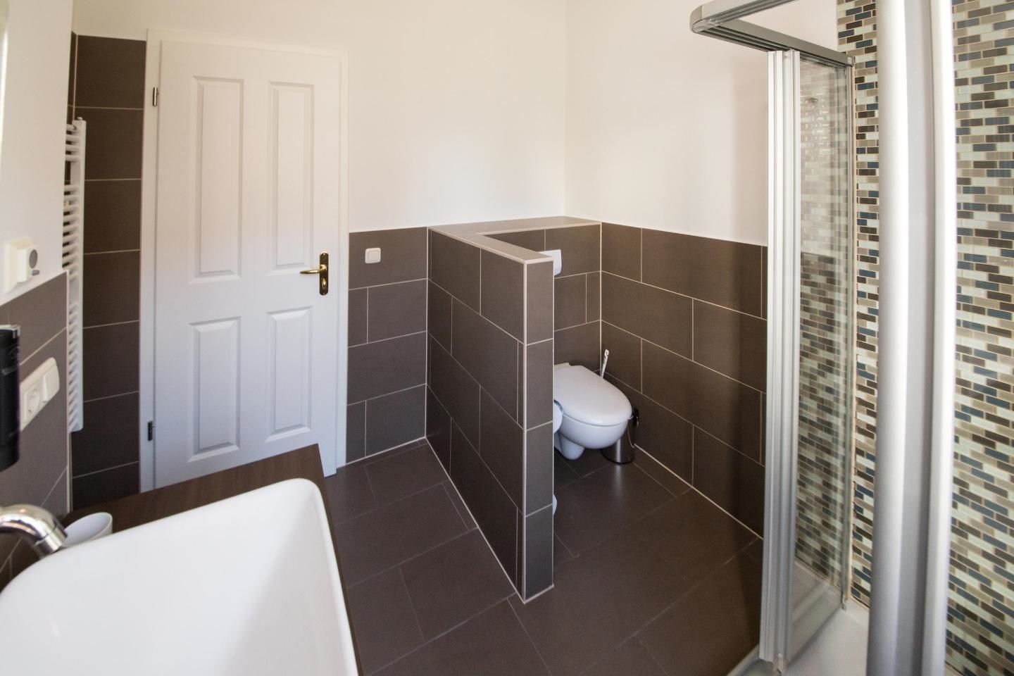 Un baño moderno con una bañera blanca, un inodoro y una zona de ducha con puerta de cristal.