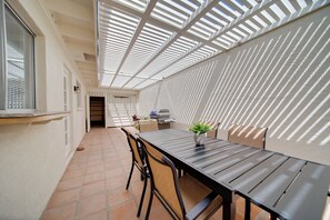 Relax in this serene patio area with a long table and four chairs, surrounded by lush greenery and natural light.