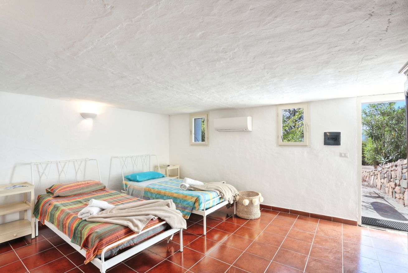 Une chambre avec deux lits, une petite table, un climatiseur fixé au mur et une vue sur la verdure.
