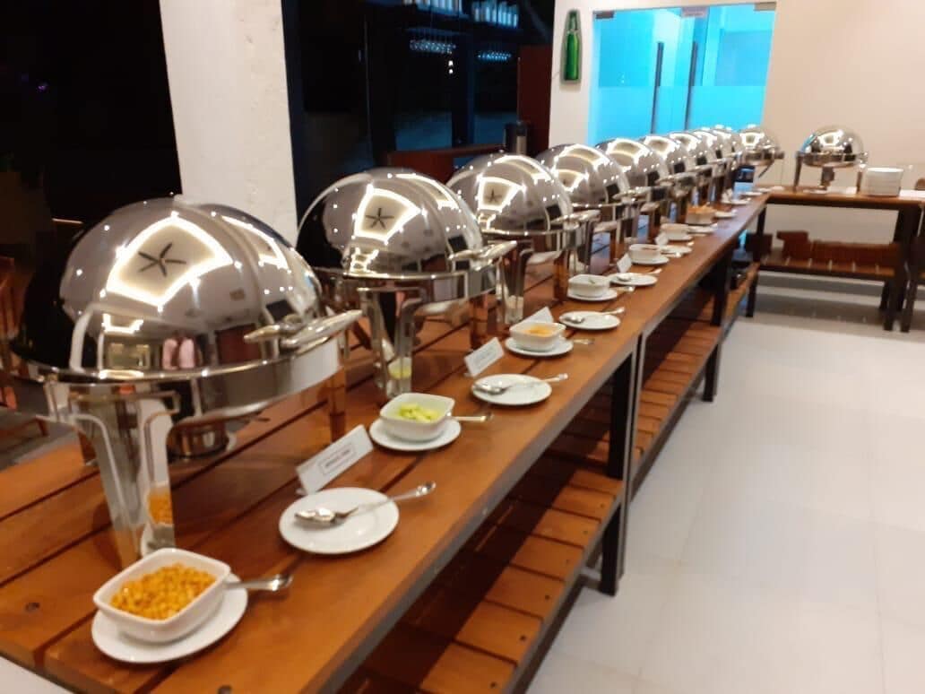 Montaje de bufé con varias estaciones de comida, cada una cubierta por una campana y señalizada con etiquetas.