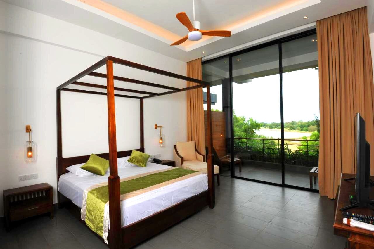 A four-poster bed with a green throw, a ceiling fan, and a large sliding glass door leading to an outdoor area with a view of greenery.