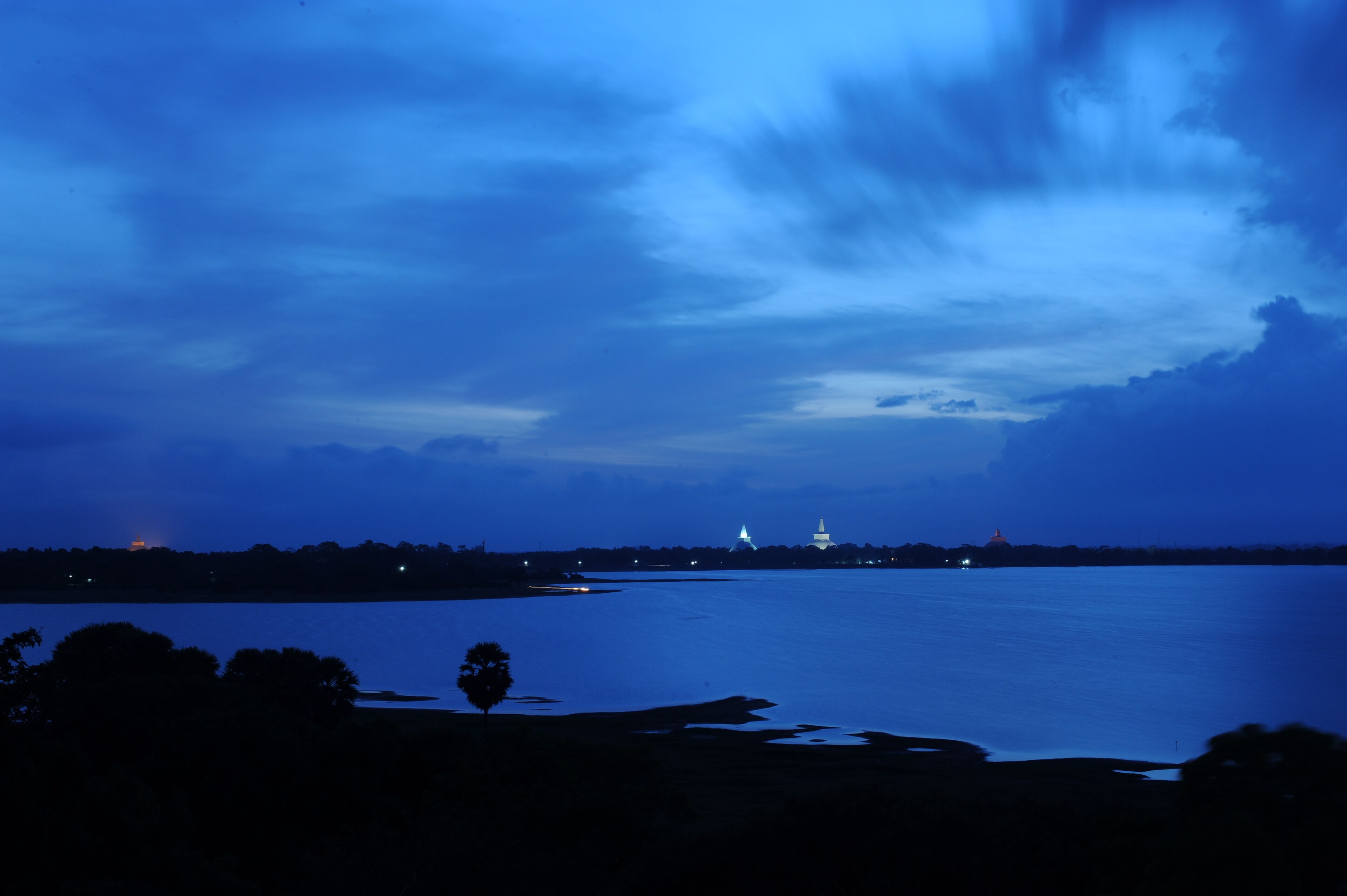 A nighttime view of a large body of water with a distant illuminated structure, likely a government building, and a lighthouse.