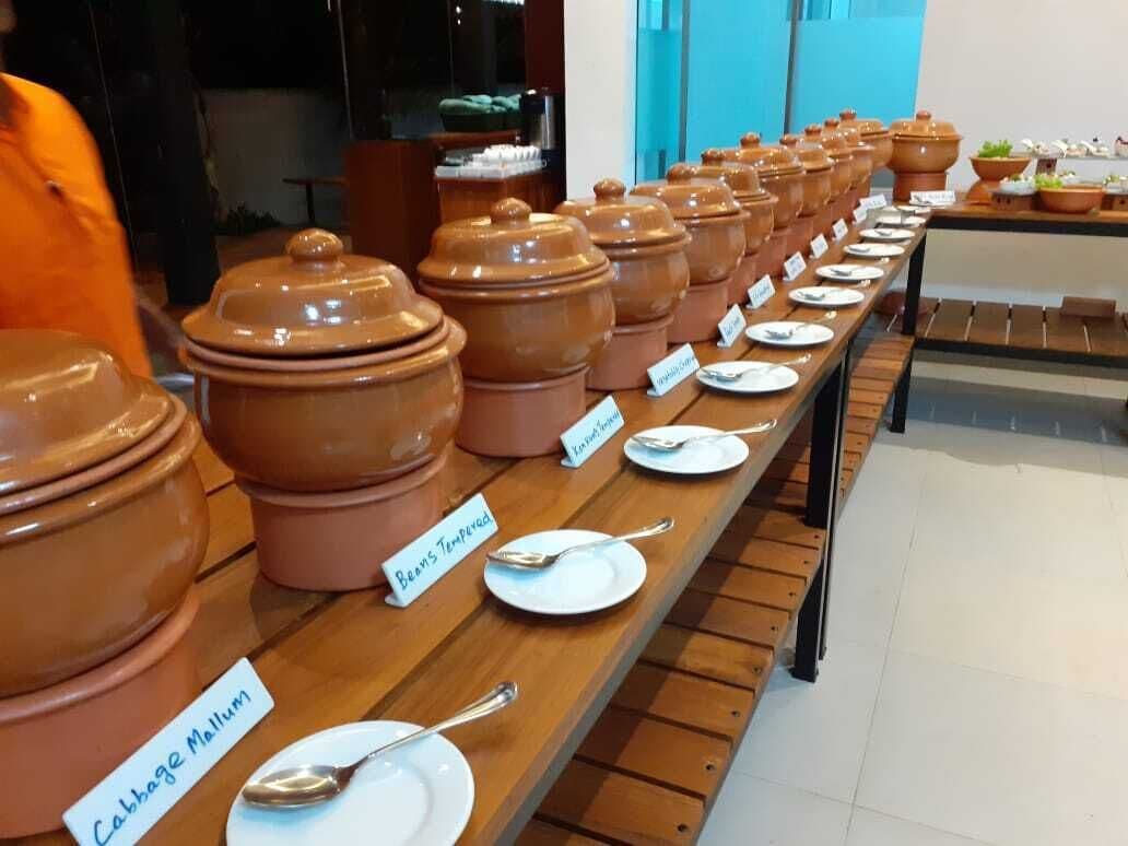 A buffet setup with terracotta pots labeled with food names like "Cabbage Mullum" and "Beef Stewed."
