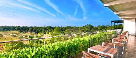 A terrace with tables and chairs overlooking a lush green landscape.