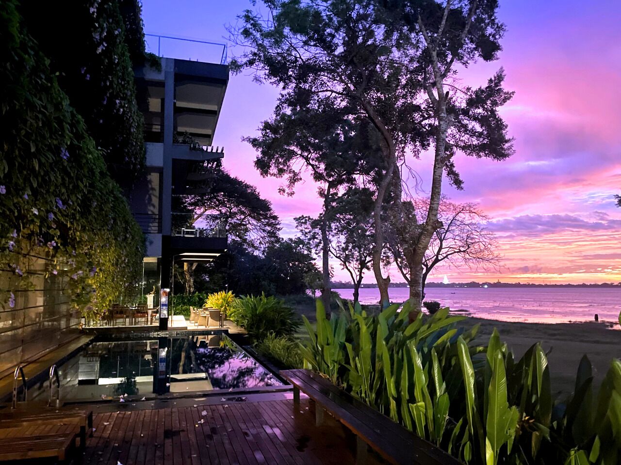A modern building with a pool area, overlooking a beach with a sunset view.