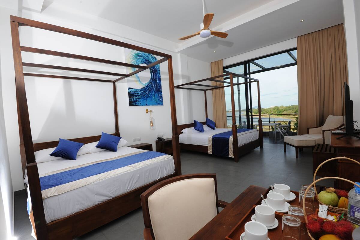 Ein Hotelzimmer mit vier hölzernen Himmelbetten, einem Esstisch mit Frühstücksangeboten und Blick ins Freie.