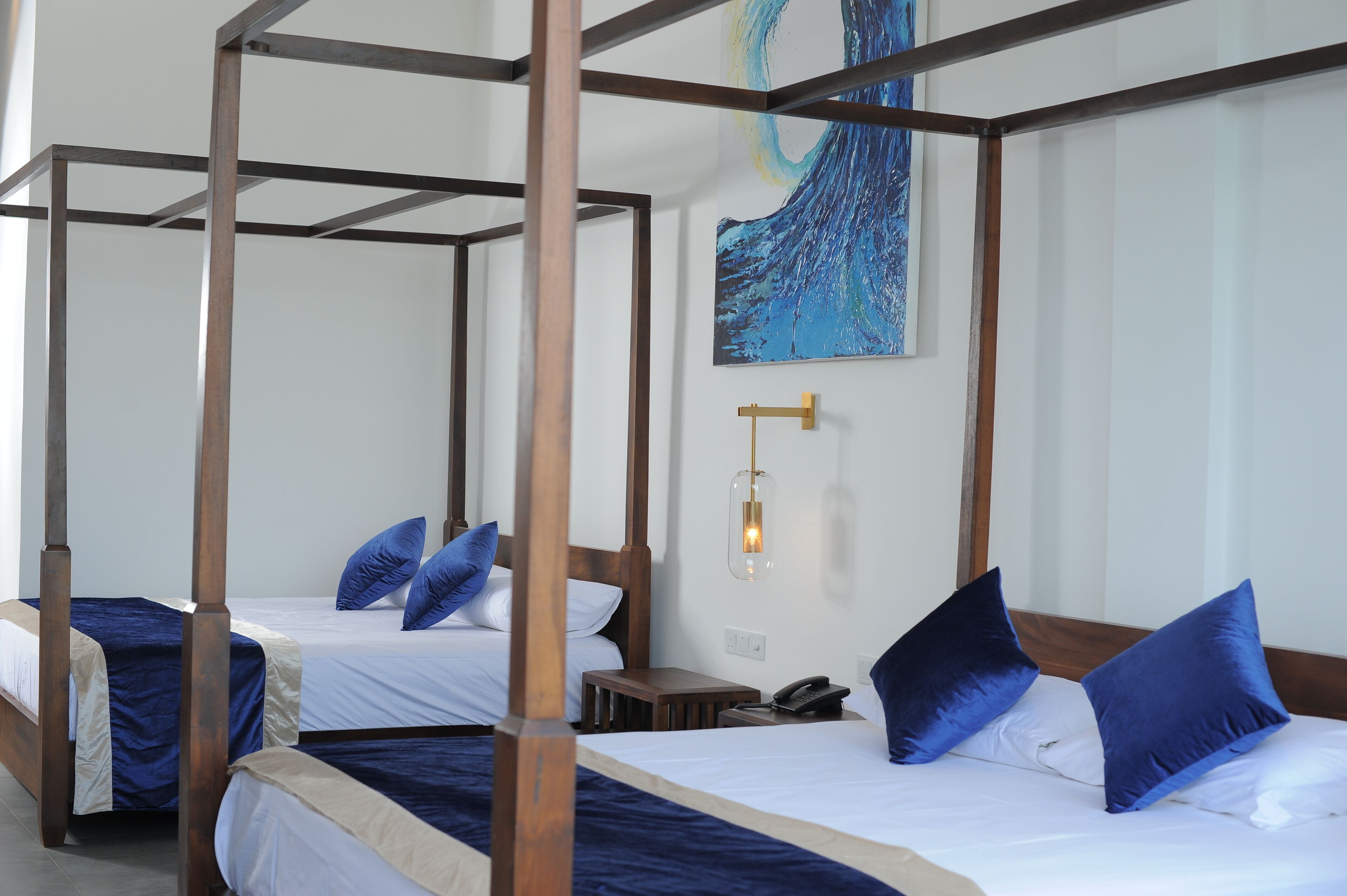 Une chambre avec un lit à baldaquin comportant deux lits, chacun agrémenté d’oreillers bleus, une table de chevet, un téléphone et un luminaire fixé au mur.