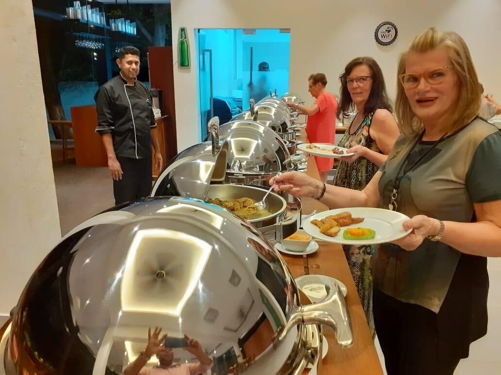A buffet setup with multiple serving stations, a person holding a plate, and another person serving food.