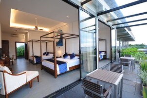 A modern hotel room with a large bed, a balcony with outdoor seating, and a view of the outdoors.