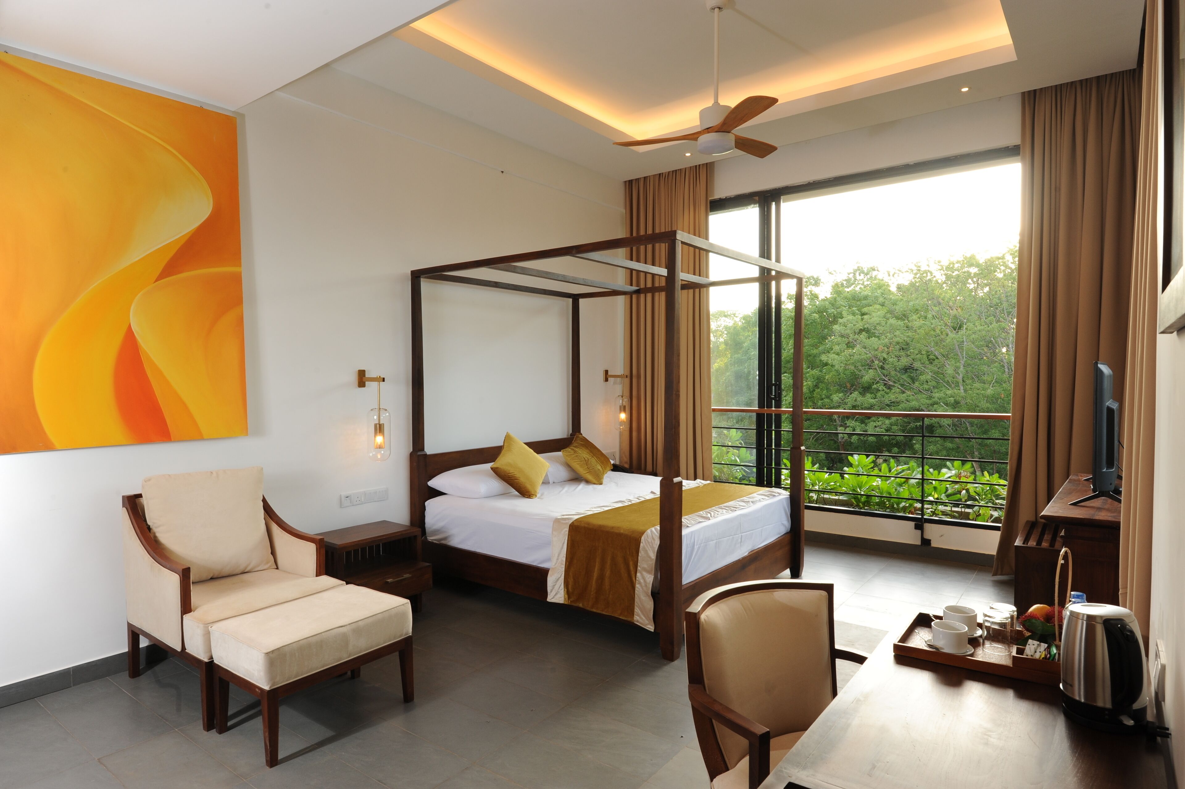 A bedroom with a four-poster bed, a chair, a bedside table, a TV, and a balcony with a view of greenery.