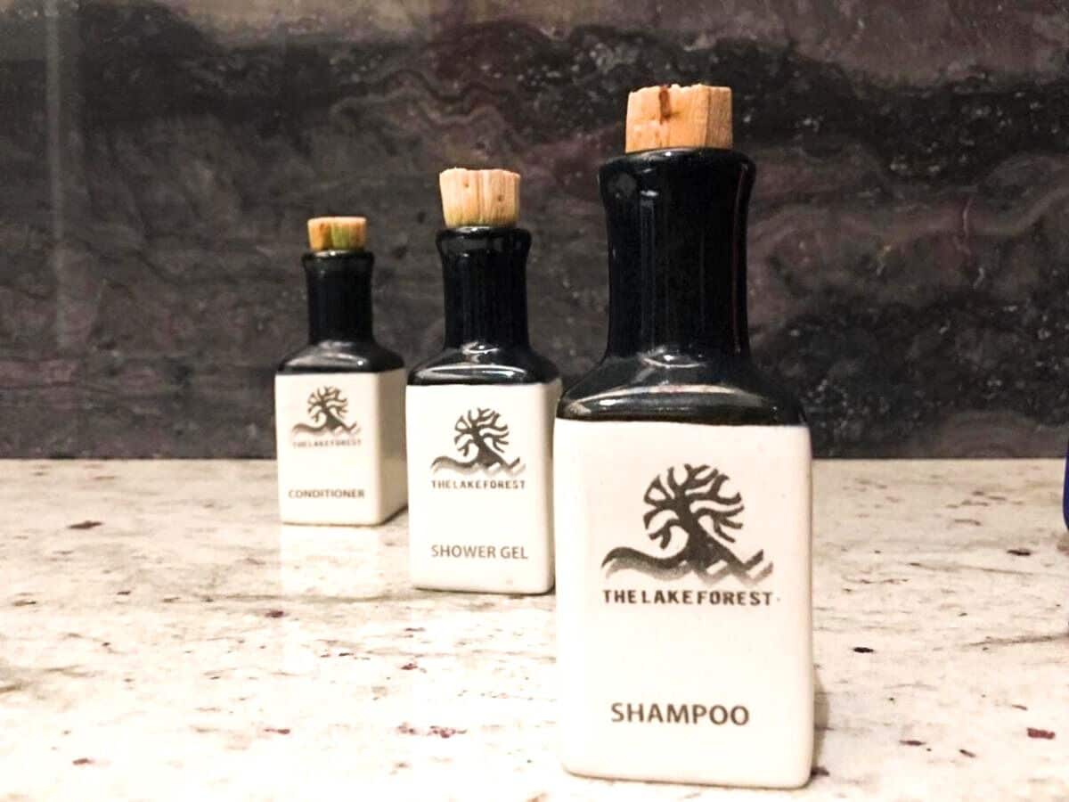 Trois flacons de shampoing, d’après-shampoing et de gel douche de la marque The Lake Forest, posés sur une surface en marbre.