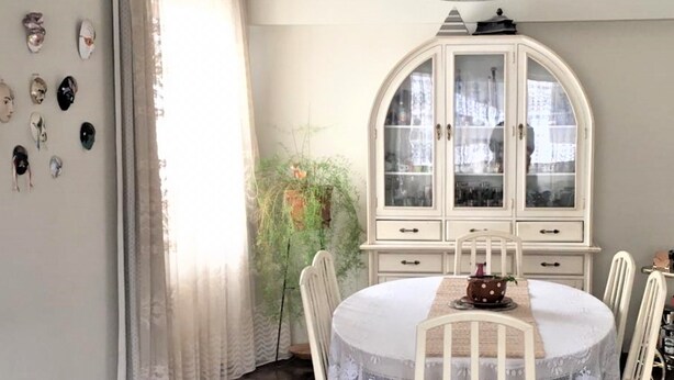 A dining area with a round table, white chairs, a white cabinet with glass doors, and a hanging light fixture. - Huancaro Familiar Apart (Cusco)