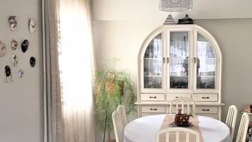 Un comedor con una mesa redonda, sillas blancas, un armario blanco con puertas de vidrio y una lámpara colgante.