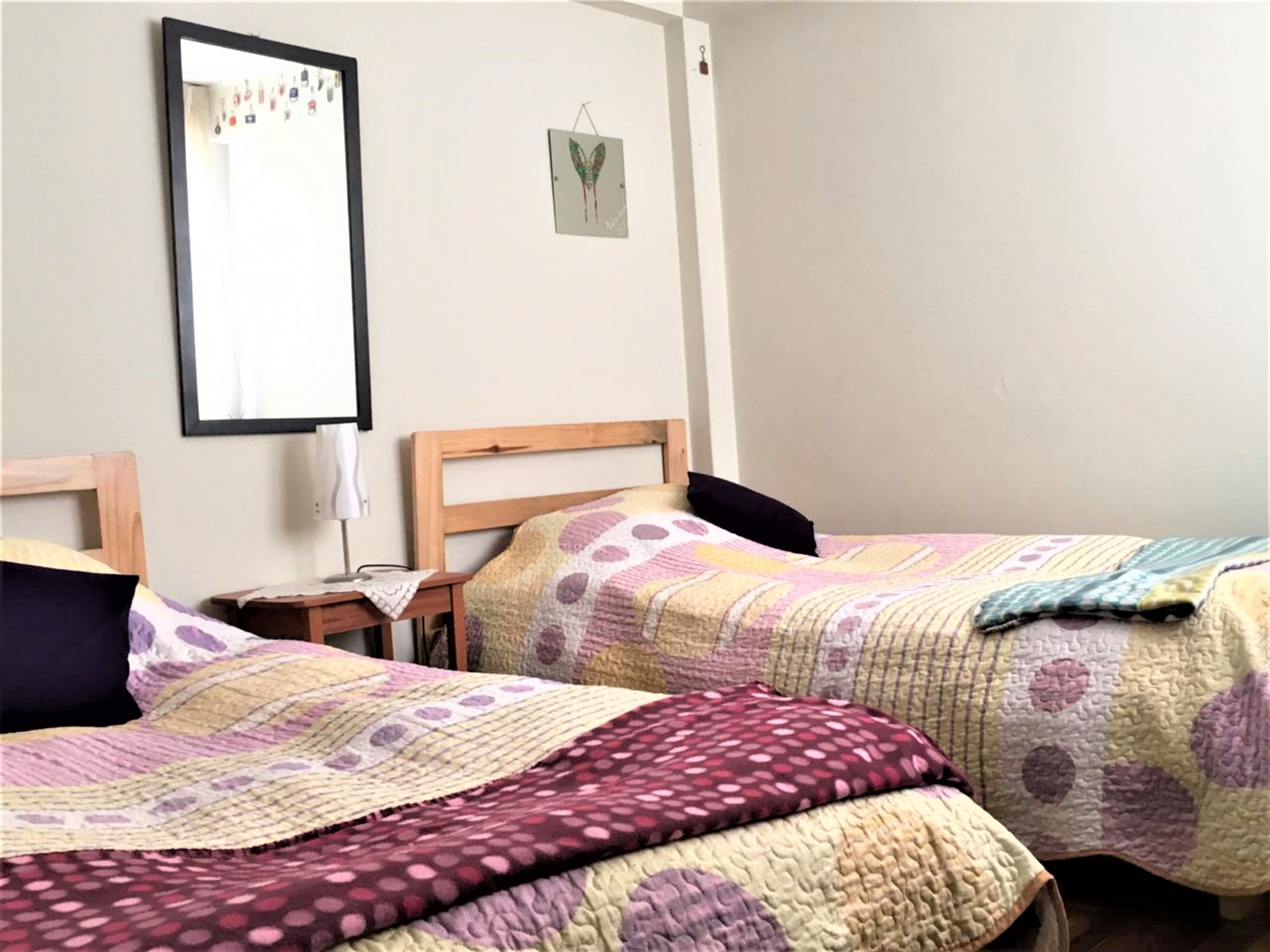 Un dormitorio con dos camas individuales, una mesita de noche con lámpara y un espejo fijado a la pared.