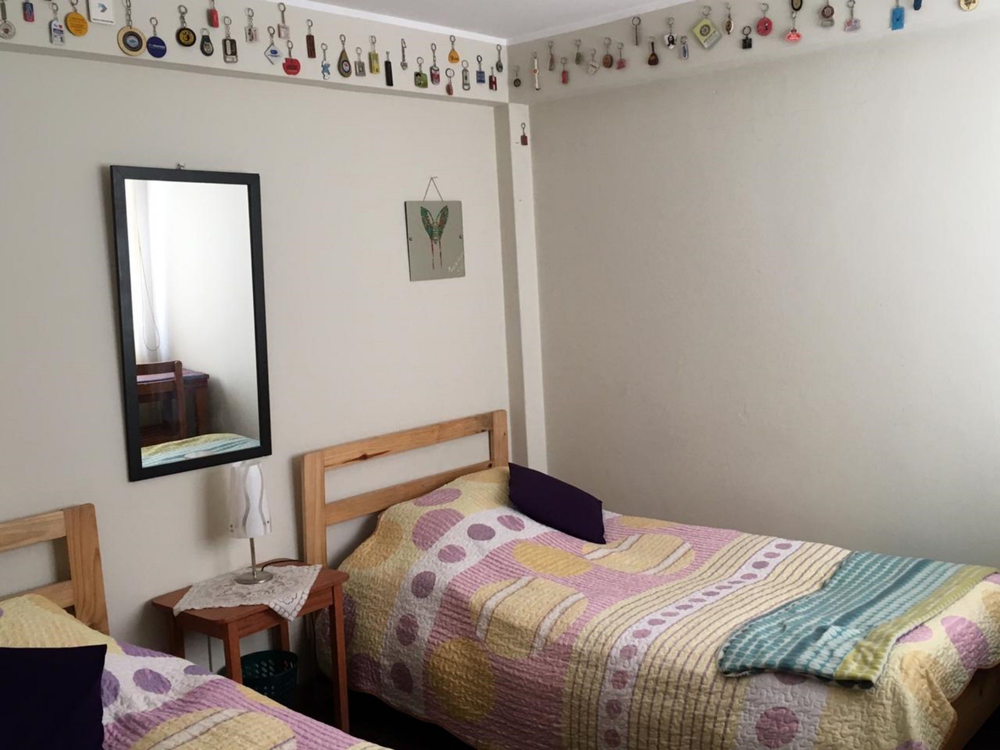 A bedroom with two single beds, a wooden headboard, a small bedside table, a mirror, and a wall-mounted key holder.