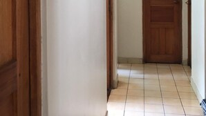 A hallway with a wooden door at the end, white walls, and tiled flooring. - Huancaro Familiar Apart (Cusco)