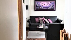 A living room with a black sofa, a coffee table, and a framed artwork on the wall. - Huancaro Familiar Apart (Cusco)