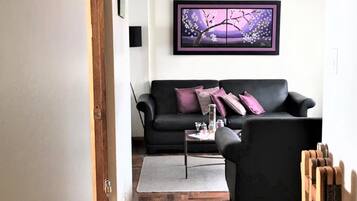 Una sala de estar con un sofá negro, una mesa de centro y una obra de arte enmarcada en la pared.