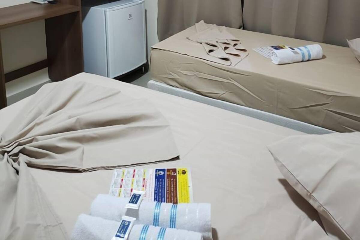 Ein Hotelzimmer mit zwei Betten, einem Kleiderschrank, einem kleinen Kühlschrank und einem Fenster mit Vorhängen.