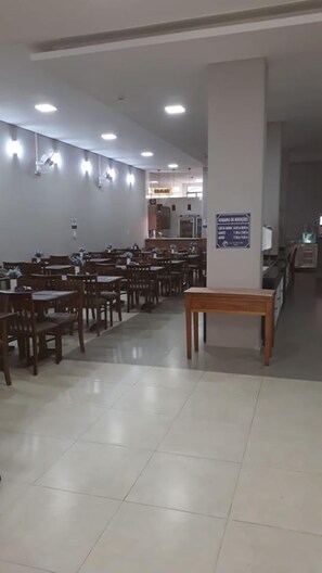 Un salón amplio con filas de mesas y sillas de madera, un pilar central y un cartel en la pared.
