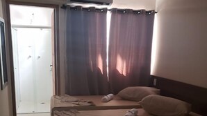 Habitación de hotel con dos camas, zona de ducha y ventana con cortinas.