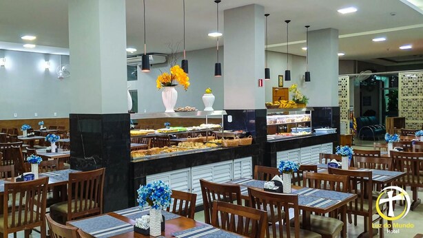 Un comedor de hotel con varias mesas y sillas, un bufé central y lámparas colgantes.