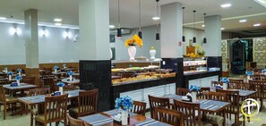 A hotel dining area with multiple tables and chairs, a central buffet, and hanging pendant lights. - Luz do Mundo Hotel (Aparecida)