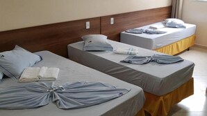 Habitación de hotel con dos camas, cada una con cubrecama gris y falda amarilla. Encima de las camas, hay un cuadro con flores en la pared.