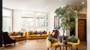 A modern lobby with yellow sofas, purple and green chairs, a large potted plant, and a wooden floor. -  DIWOTEL by Trip Inn Frankfurt Airport Dreieich (Dreieich)