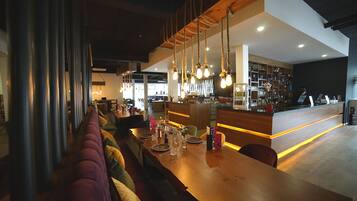 A modern restaurant with a long wooden bar, cushioned seating, and hanging light fixtures.