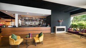 A modern bar area with a wooden counter, seating with yellow chairs, and a fireplace. -  DIWOTEL by Trip Inn Frankfurt Airport Dreieich (Dreieich)