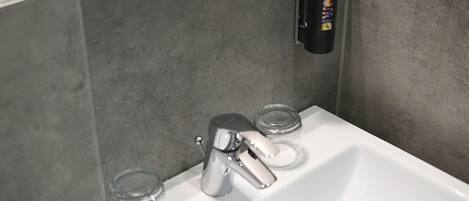 Un lavamanos de baño con un grifo moderno, un dispensador de jabón y dos jaboneras de vidrio transparente.