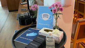 A reception area with a desk, a digital screen, a hand sanitizer dispenser, a sign for mask usage, and a water bottle.