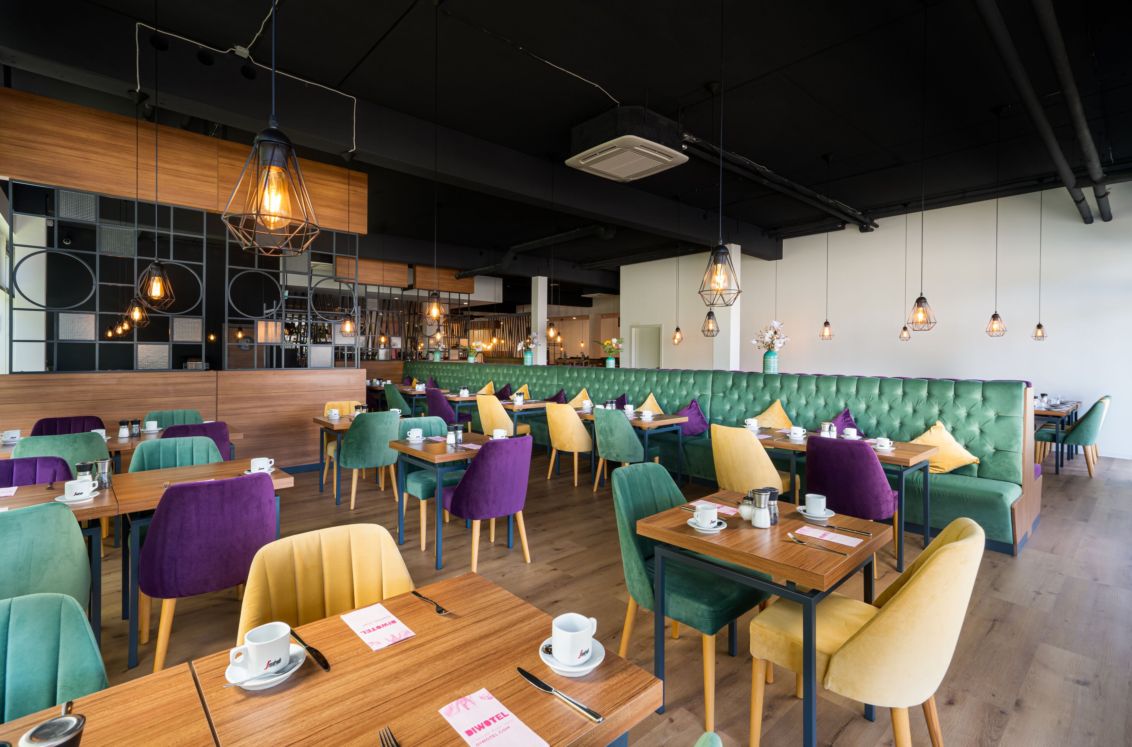Un café moderno con mesas de madera, sillas coloridas y asientos acolchados de color verde.