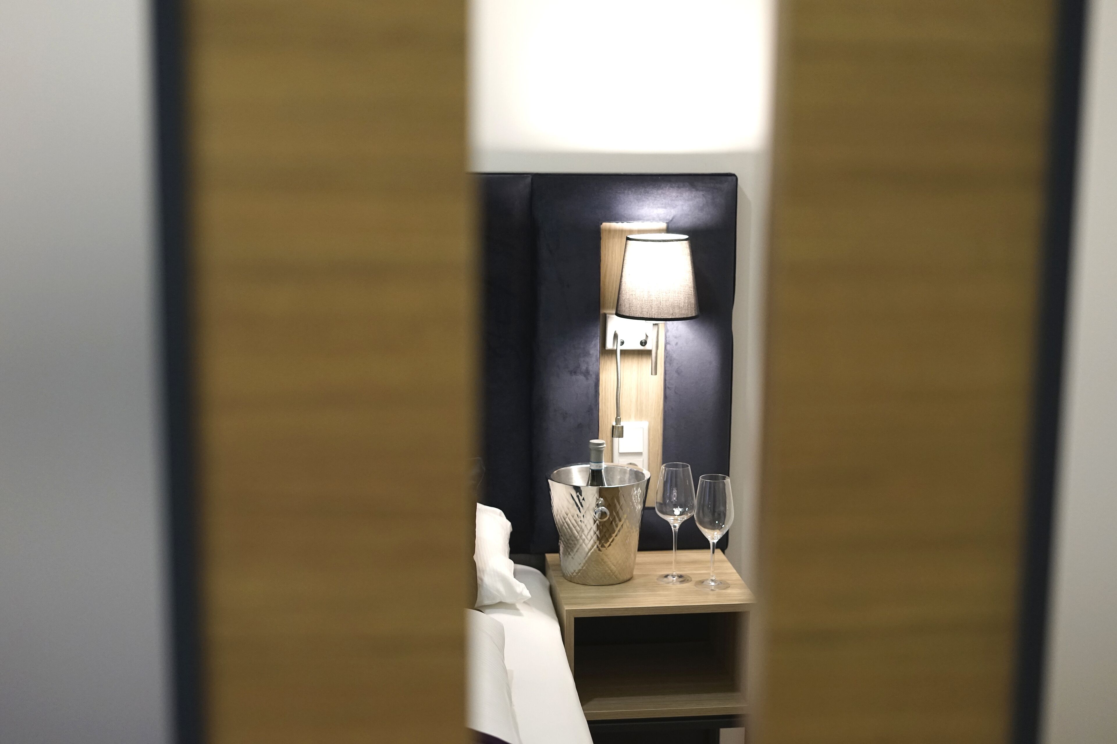 Ett hotellrum med ett nattduksbord, en lampa, en hink och två glas.