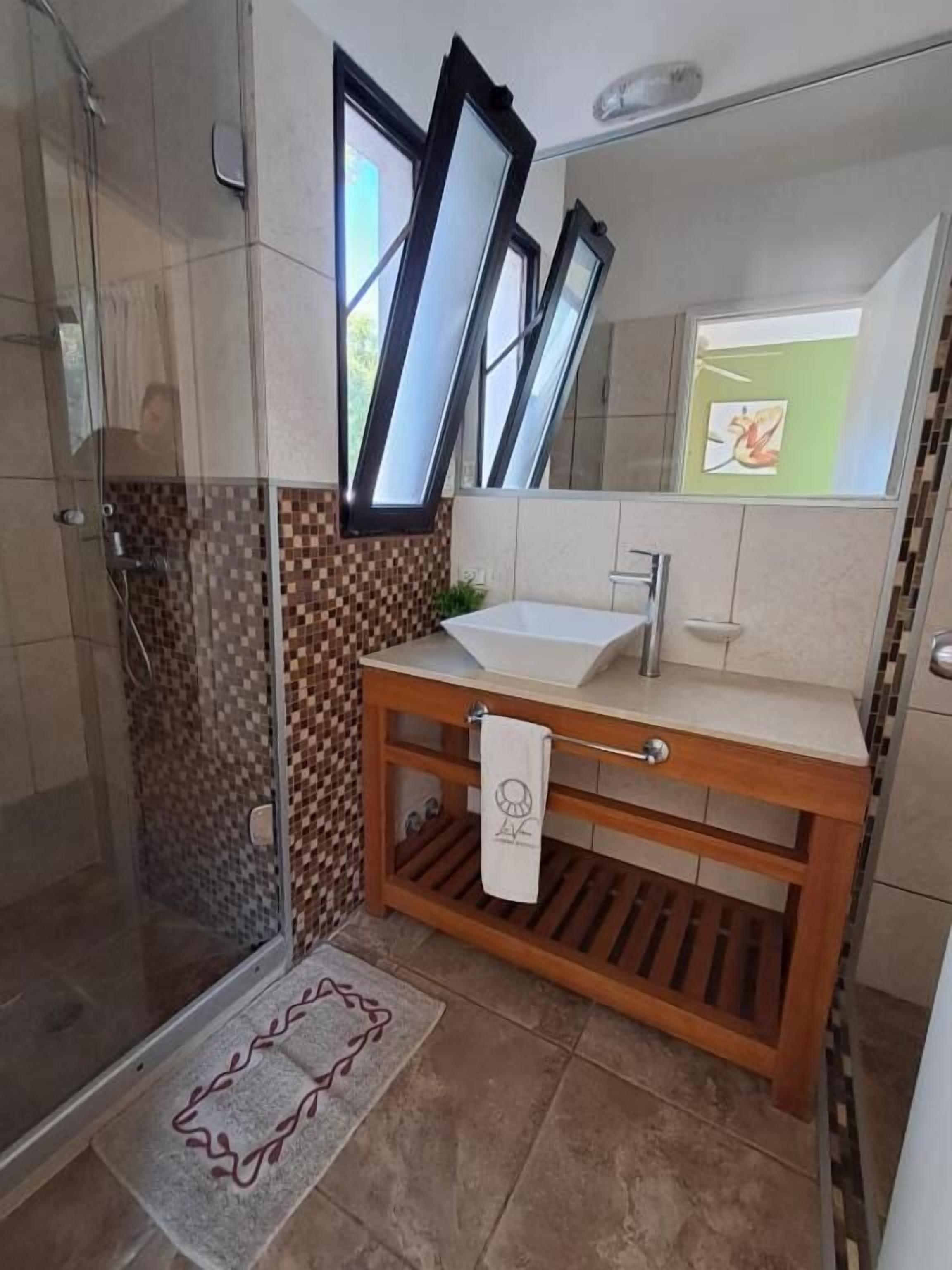 Un baño con cabina de ducha de vidrio, un tocador de madera con lavamanos y un espejo con marco.