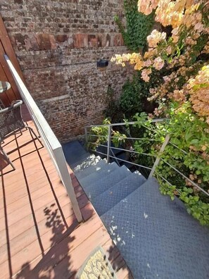 A wooden deck with a metal railing, a brick wall, and a staircase leading to a lower level.