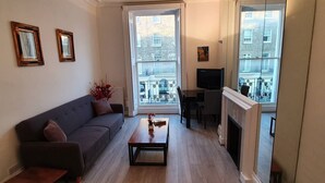 A living room with a sofa, coffee table, fireplace, and large windows with a view of buildings.