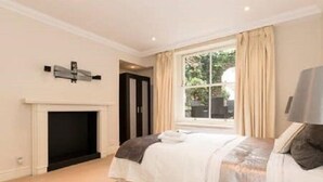 A bedroom with a bed, a fireplace, a window with curtains, and a wall-mounted light fixture.