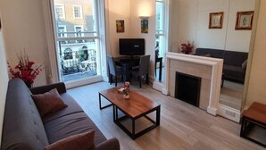 A living room with a sofa, a coffee table, a fireplace, a television, and a balcony with a view of buildings.